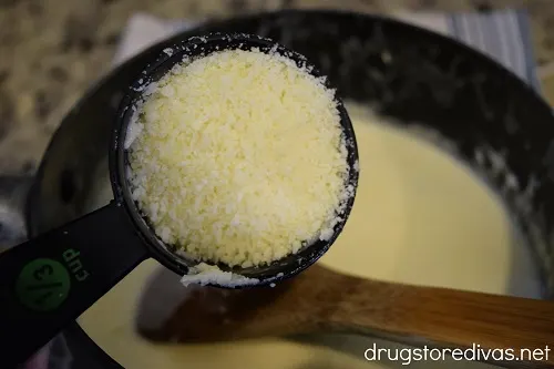 Parmesan cheese being poured into alfredo sauce.