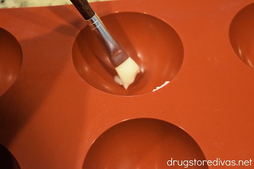 A paint brush being used to "paint" melted white chocolate into a dome silicone mold.