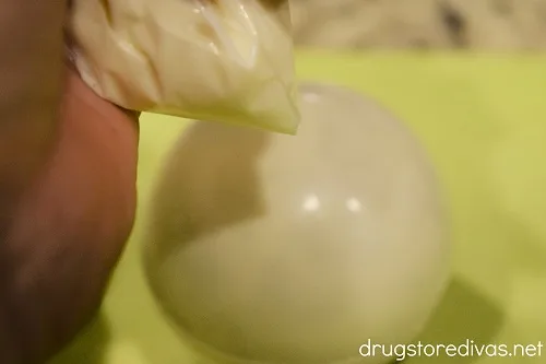 Melted white chocolate in a bag above a white chocolate ball.