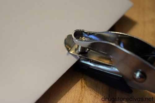 A hole puncher punching a hole in white card stock.