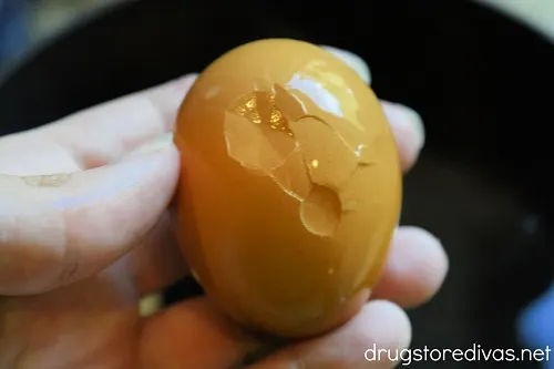 A hand holding a hard boiled egg with a cracked shell.
