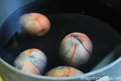 Four hard boiled eggs in a bowl of water with red and blue food coloring.