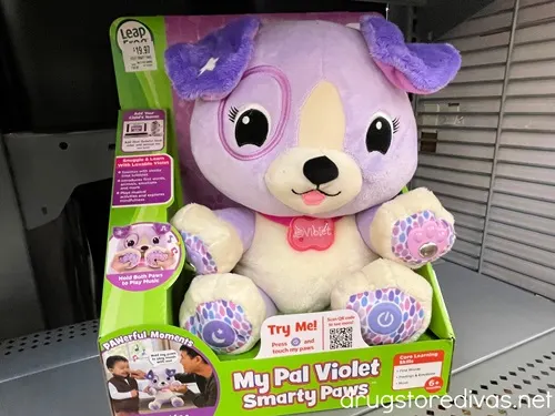 A purple bear, which is the Leapfrog My Pal Violet toy, in a box on a shelf.