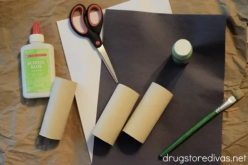Toilet paper rolls, glue, scissors, white and black construction paper, green paint, and a paint brush.