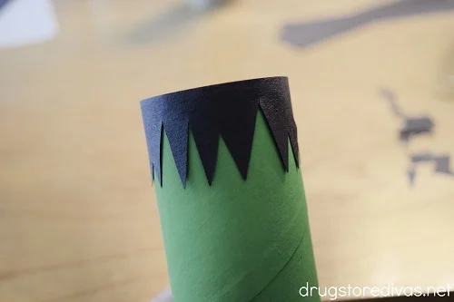 Construction paper hair glued onto a green toilet paper roll.