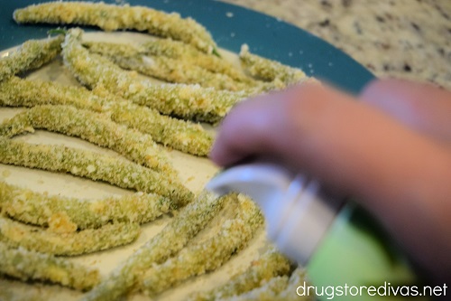 Raw panko and parmesan green bean fries on a plate being sprayed with avocado oil.