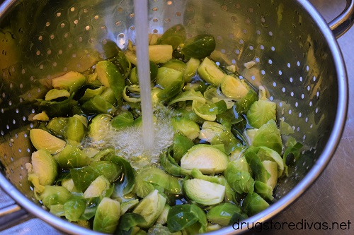 Brussels sprouts in a colander under running water.