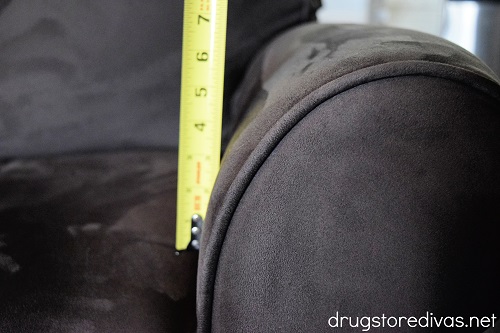 A tape measure measuring the arm of a couch.