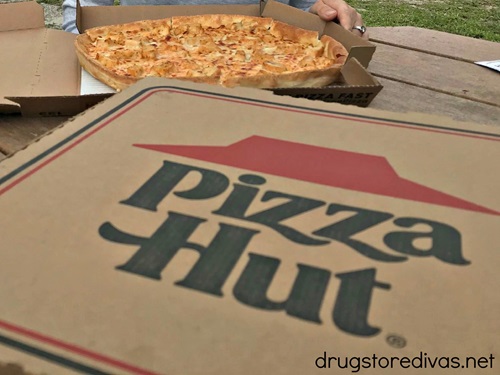 A pizza in a box in the back and a closed Pizza Hut box in the front.