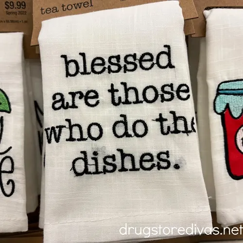 A tea towel that says blessed are those who do the dishes on a shelf.