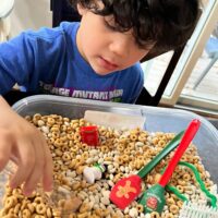A young boy playing in a sensory bin with the words 