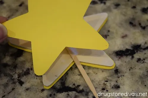 A yellow card stock star being glued onto a wooden star.