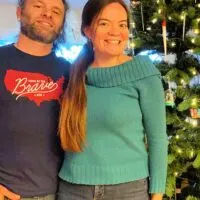 A couple standing in front of a Christmas tree with the words 