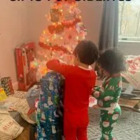 Two boys opening Christmas gifts in front of a Christmas tree with the words 