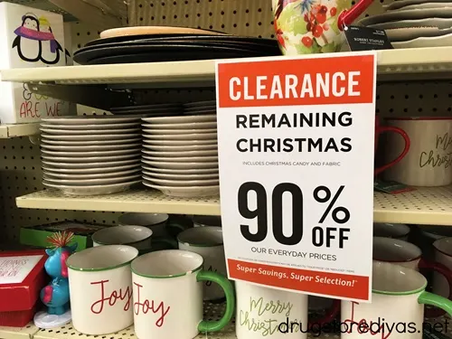 A sign advertising 90% off remaining Christmas items with cups, mugs, and more behind it.