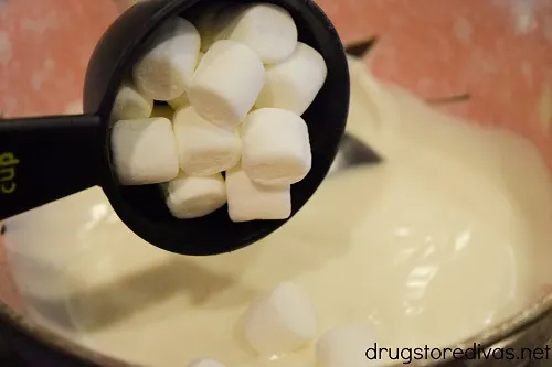 Mini marshmallows being poured into melted vanilla almond bark.
