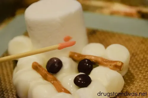 An orange nose being painted on a melted snowman marshmallow candy.