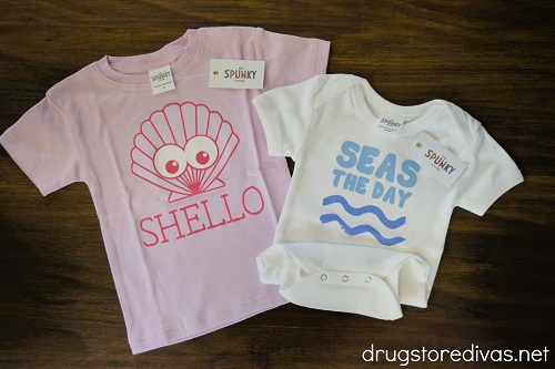A pink shirt with a shell that says "Shello" and a white onesie that says "Seas The Day" with two waves under it.
