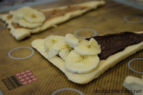 Two crescent rolls rolled out, one is topped with Nutella and one is topped with peanut butter, both have banana slices.