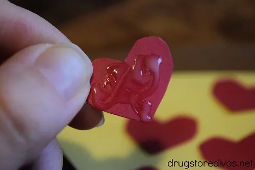 Fingers holding a red heart with glue on it above a pizza piece cut from card stock.