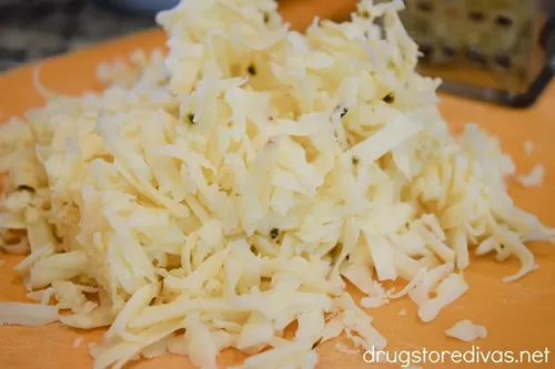 Shredded white cheese on an orange cutting board.
