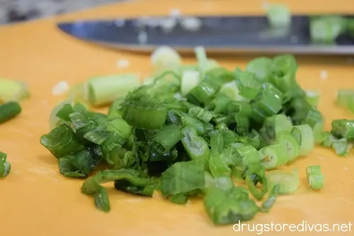 Chopped green onions on an orange cutting board with a knife in the background.