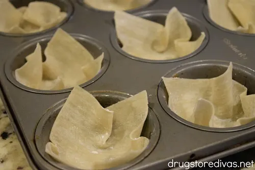 Wonton wrappers in the cavities of a muffin pan.