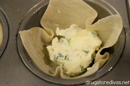 Wonton wrappers with a scoop of jalapeno popper filling in the cavities of a muffin pan.