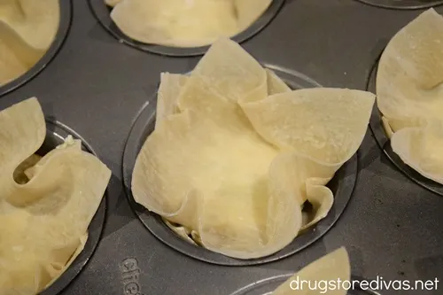 Wonton wrappers in the cavities of a muffin pan.
