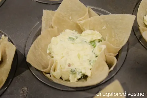 Wonton wrappers with a scoop of jalapeno popper filling in the cavities of a muffin pan.
