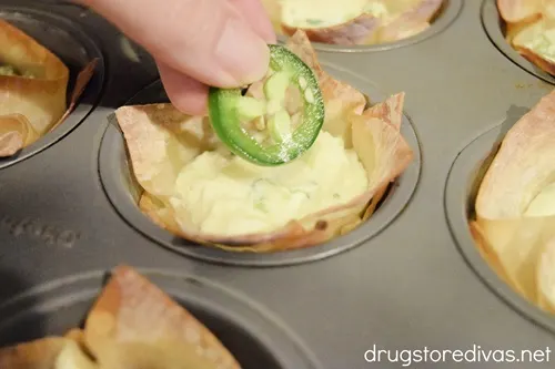 A hand putting a slice of jalapeno on the top of a jalapeno pepper wonton cup.