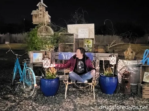 A woman sitting on a bench touching a lamp surrounded by outdoor decorations at the Madd Hatters Haunt in Union Gap, Washington.