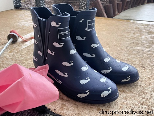 A pair of blue rain boots with whales on them next to a pink umbrella.