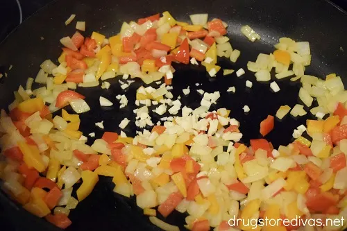 Garlic, red pepper pieces, orange pepper pieces, and onion pieces in a skillet.