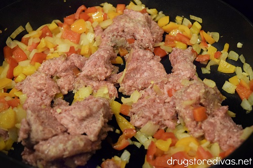 Ground sausage, red pepper pieces, orange pepper pieces, and onion pieces in a skillet.