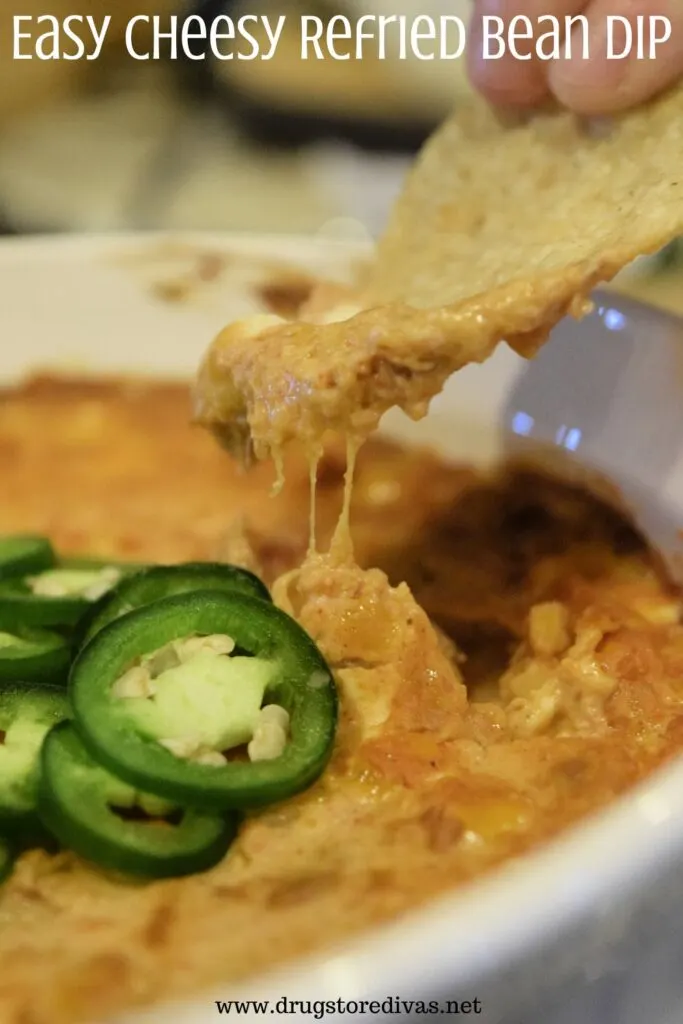 A tortilla chip coming out of bean dip with the words "Easy Cheesy Refried Bean Dip" digitally written on top.