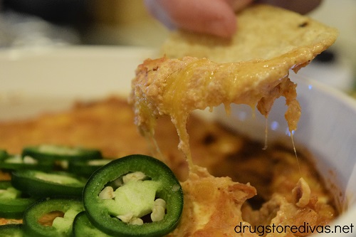 A chip being pulled out of a bowl of easy cheesy refried bean dip.