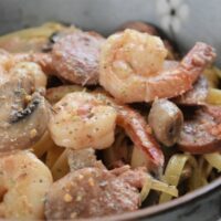 Shrimp, sausage, mushrooms, and pasta in a bowl with the words 
