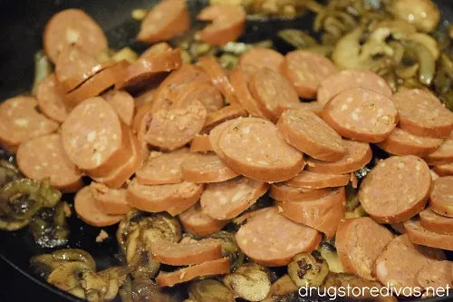 Sliced sausage in a pan with mushrooms and onions.