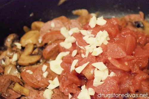 Diced tomatoes and onions in a pan with sausage, mushrooms, and onions.
