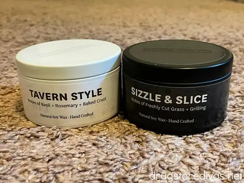 Two pizza scented candles, one white and one black, next to each other.