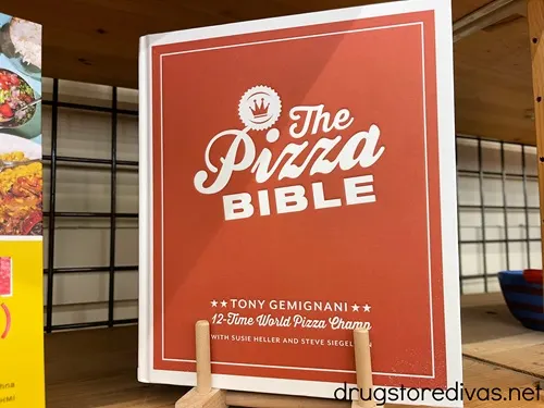 The Pizza Bible book, which is a red book with white words and a white trim, on the shelf in a store.