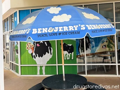 A table with an umbrella in front of a Ben & Jerry's scoop shop.