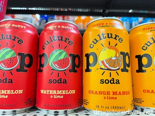 Four cans of Culture Pop soda, two red and two orange, on a shelf.