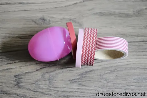 A pink plastic egg and four rolls of pink and red washi tape.