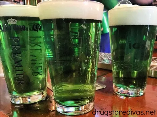 Three pint glasses on a bar filled with green beer.