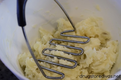 A potato masher mashing potatoes in a bowl.