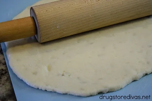 Dough, on a blue cutting board, with a rolling pin on top.