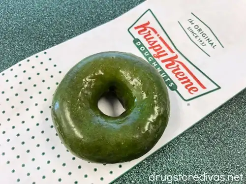 A green doughnut on top of a Krispy Kreme doughnuts bag.