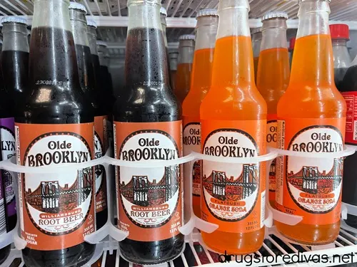 Four bottles of Olde Brooklyn Soda, two root beer and two orange, on a fridge shelf.